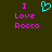 Dark green background with pink text reading "I Love Rocco" and a cyan pixelated heart symbol above the right side of the text.