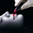 Static image of a person's face with lips being applied with red lipstick by gloved hands against a black background.