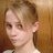 Pixelated close-up of a person with light brown hair tied back, wearing a white top against a warm-toned background.