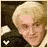 A pixelated image of a person with light blonde hair and fair skin, wearing dark clothing against a dark background.