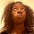 Pixelated image of a person with long brown hair, light skin tone, and closed eyes looking upward against a beige background.