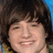 Pixelated close-up of a person with dark brown hair and a light skin tone smiling, set against a blue and green background.