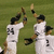 Baseball players in white uniforms with black numbers high-fiving on a grass field, captured across showing motion progression