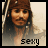 Pixelated image of a person with long hair and a headband, wearing light-colored clothing against a pale background.