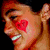 A person with short dark hair has a red heart-shaped mark on their cheek, then holds a white object near their mouth.