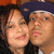 Two people in close proximity, one wearing a dark blue cap, both with light skin tones and smiling expressions.