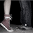 Pixelated close-up of two legs in motion, one wearing a light-colored sock and brown shoe, the other in dark pants and black shoe against a dark background.