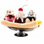 A banana split dessert with multiple scoops of ice cream, toppings, and a cherry on top sits in a glass dish.