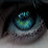 A pixelated close-up of a stylized eye with teal and green irises, dark pupil, and blurred background.