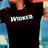 A person wearing a black shirt with white text and blue sleeves, standing against a blurred background.