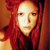 Pixelated portrait of a person with long red hair against a warm-toned background, wearing dark clothing with visible texture.