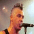 A pixelated image split into two sections: a person with short hair holding a microphone on the left, and a red geometric symbol on black background on the right.