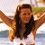 A pixelated figure with long dark hair stands with arms raised against a blurred background of light and green tones.