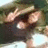 Pixelated image of a figure with light skin tone, dark hair, and a dark top, holding a light-colored object near the face against a blurred background.