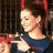 A pixelated image of a person with dark hair tied up, wearing red headbands and a blue top, holding an object near their chest against a dark background.