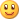 Pixelated yellow smiley face with brown eyes showing white pupils and dark red irises, a wide red mouth forming a grin, set against a gray background.