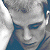 A pixelated image of a person with light hair and blue eyes, wearing a dark shirt against a green background with bright green text.