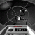 Pixelated grayscale image of a character in a dark suit with a white tie, standing behind a control panel with buttons and a red indicator light.