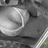 Pixelated grayscale image of a stylized object with curved white and gray shapes against dark background, featuring a small yellow pixel cluster near bottom right.