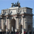Pixelated image of a large stone archway with columns under a clear blue sky, featuring a central archway and smaller side arches.