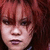 Pixelated close-up of a person with reddish-brown hair and dark eyes, mouth slightly open, against a dark background.