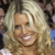 A pixelated close-up of a person with light-colored hair, smiling broadly with visible teeth, set against a blurred background.