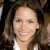 A static pixelated image shows a person with long brown hair wearing a white top, smiling with visible teeth against a dark background.