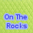 Static image with green background and blue text reading "On The Rocks" on left, horse in motion on right.