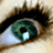 A close-up of a human eye with green and blue irises, dark eyelashes, and visible skin texture around the eye.