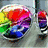 Animated icon shows a rainbow-colored object with blue and purple sections rotating inside a metallic container, while two pixelated dinosaurs with heart-shaped thought bubbles stand on a white background.