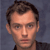 Pixelated close-up of a person's face with short brown hair against a dark blue background, static image.