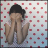 A person in a white polka-dot dress covers their face with both hands against a light blue background with red polka dots, with text above reading "AND SOMETIMES SHE CRIES ABOUT YOU".