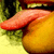 A pixelated close-up of a character's mouth and tongue, with a yellowish-orange lower face and greenish background elements.