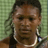 Pixelated close-up of a person with dark hair and light skin wearing a white necklace against a green checkered background.