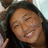 Pixelated close-up of a smiling person with dark hair, wearing a dark top, against a light background.