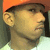 Pixelated close-up of a person's head and shoulders with orange hair, dark sideburns, light skin tone, wearing a white shirt against a blurred background.