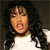 Pixelated close-up of a person with long dark hair wearing a white top against a dark background.