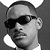 Black-and-white image of a person with short hair and dark sunglasses, wearing a white collared shirt against a gray background.