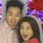 Two people pose together against a purple and red patterned background with visible pixelation.