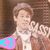 A person in a brown jacket and white shirt holds up two hands with fingers forming 'OK' signs, while colored triangular icons change color across frames.