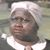 Pixelated image of a person wearing a white head covering and white collar, with a blurred background.