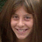 Pixelated close-up of a smiling person with long brown hair against a dark background.