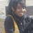 Pixelated static image of a person with dark hair wearing a black jacket over a yellow shirt, smiling slightly against a blurred background.