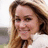 Pixelated close-up of a person with long brown hair wearing a light-colored top, set against a blurred background.