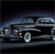 Pixelated image of a dark-colored vehicle with visible headlights and a circular emblem on the front, set against a dark background with blue and gray tones.