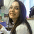 Pixelated static image of a person with long dark hair wearing a light-colored top, smiling slightly against an indistinct background.