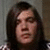Pixelated close-up of a person with long dark hair against a muted gray-brown background.