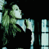A woman with long blonde hair in a black top exhales smoke, forming changing shapes like hearts and spirals against a -patterned background