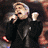 A pixelated image shows a person in dark clothing holding a microphone, with a blue circular logo containing stylized text on the right.
