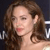 A pixelated close-up of a person with long brown hair, light skin, and red lips, set against a dark background with partial white text.